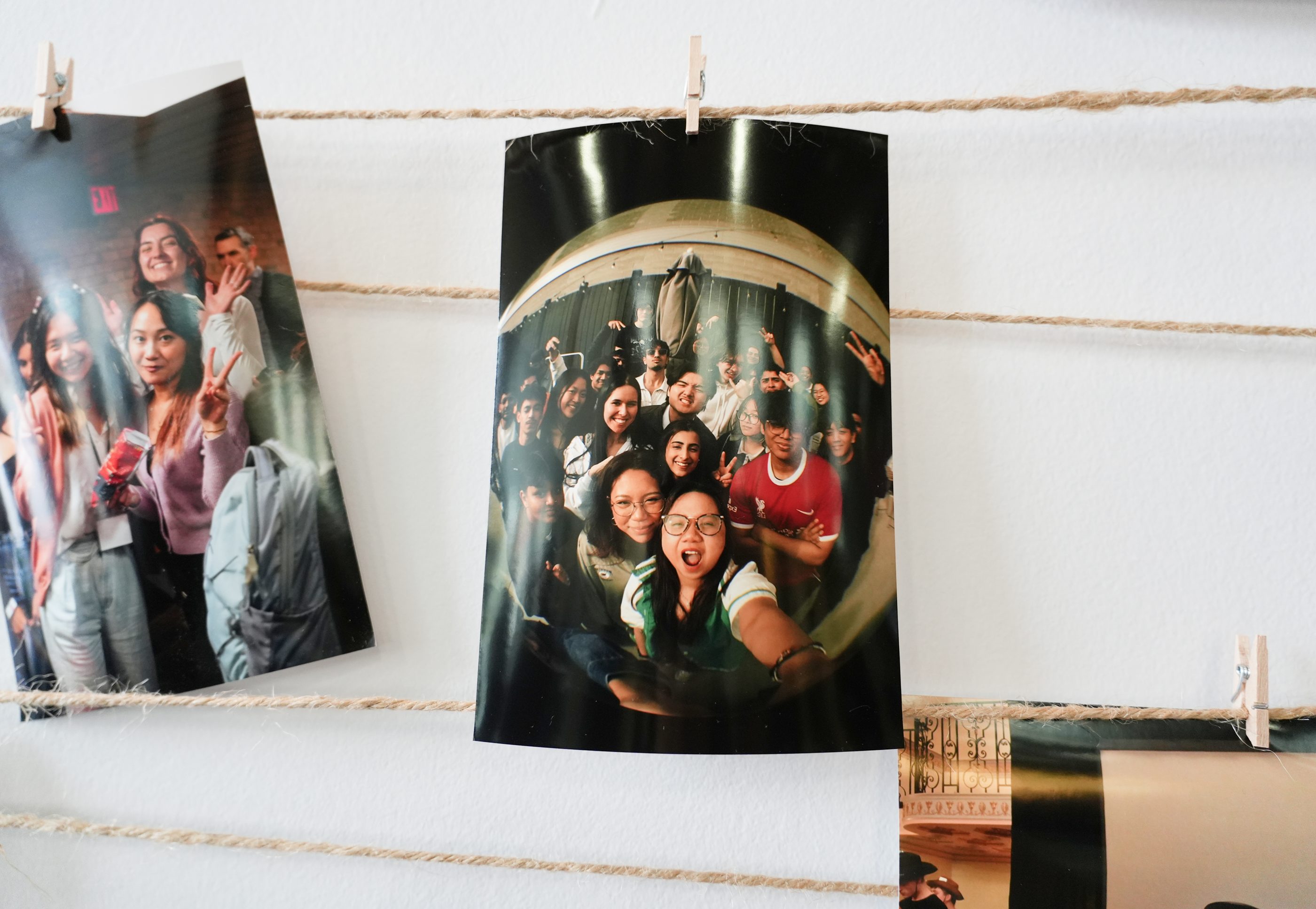 Photo prints hanging from a string against a white wall.