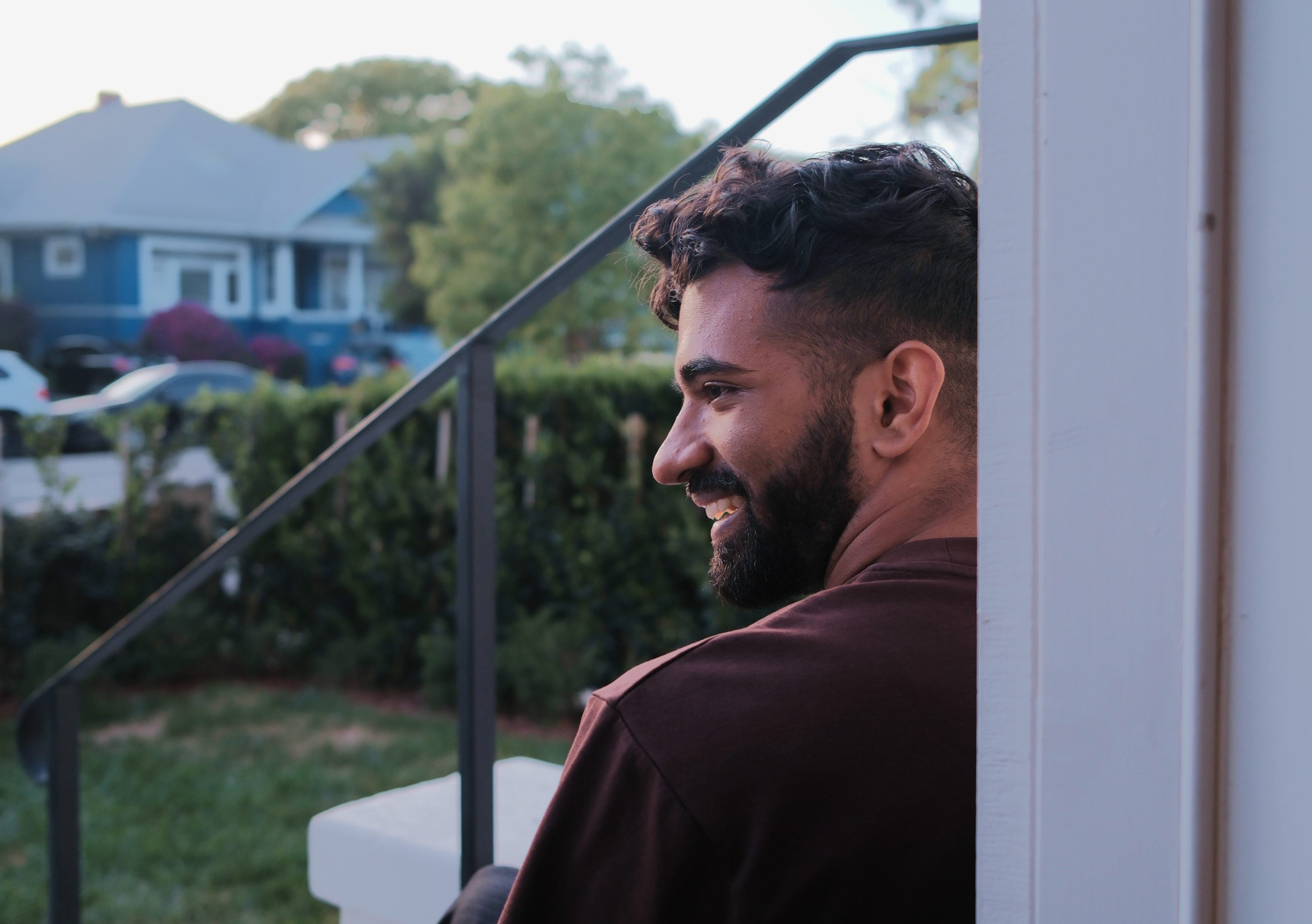 A man smiling on the front steps of a blue house.