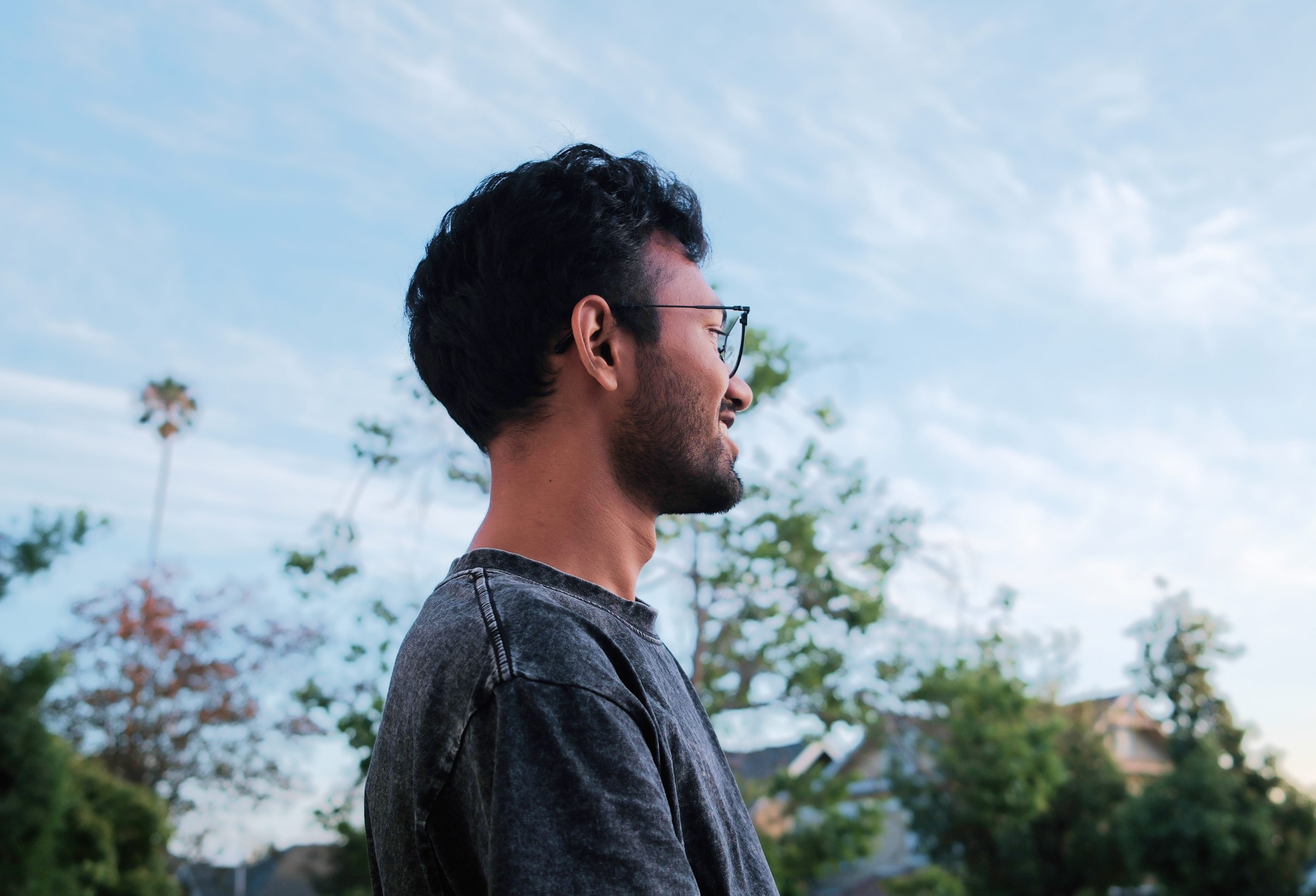 A man in glasses in profile against trees and sky.